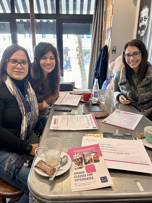 a small group of French language learners posing in a typical café in Neuilly-sur-Seine, sitting at a high table with their French learning materials and cups of coffee in front of them.